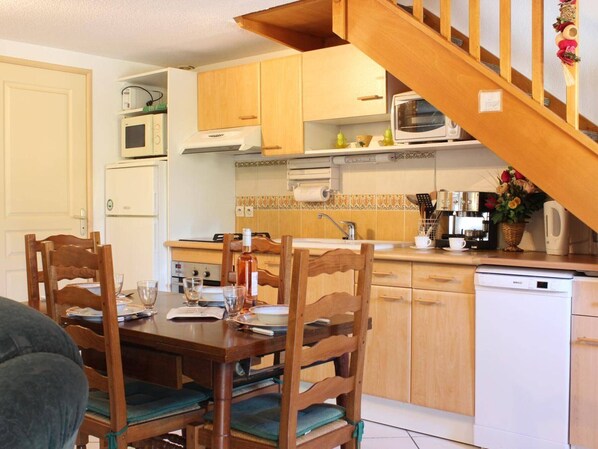 A compact kitchen with wooden cabinets, a dining table with chairs, a microwave, a stove, and a coffee maker.