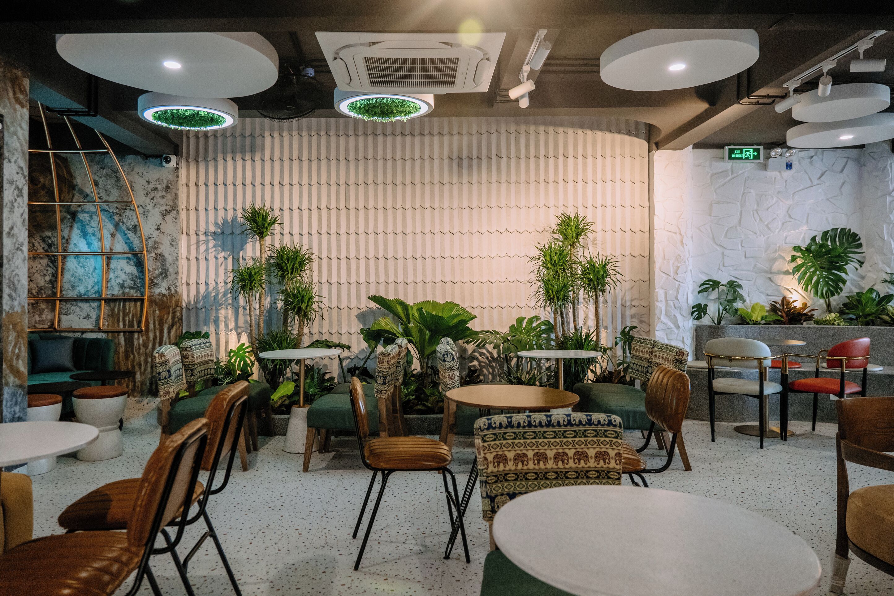 Un café moderno con mesas y sillas redondas, y una variedad de plantas.