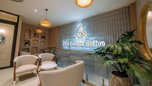 A modern coffee shop interior with comfortable seating, a prominent coffee cup logo, and a large potted plant. - La Beaute Hotel Quy Nhon (Quy Nhon)