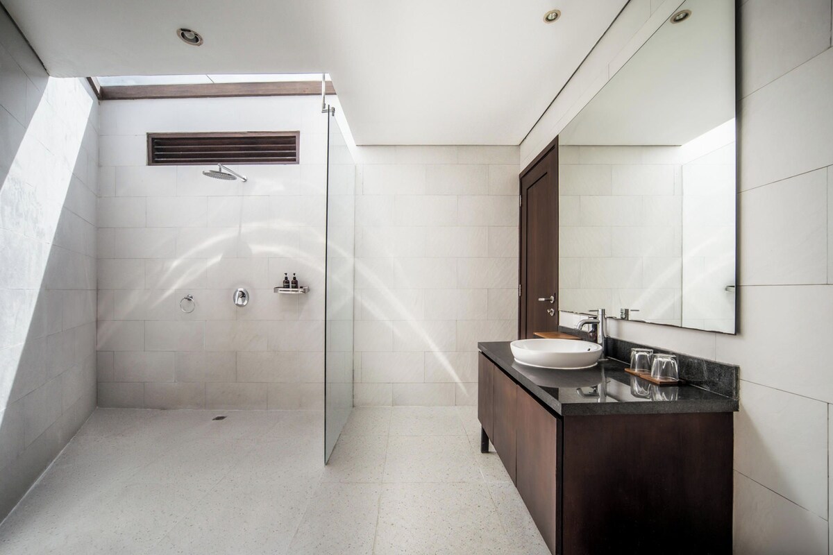 Un baño moderno con ducha envuelta en vidrio, tocador de madera oscura y un espejo grande.