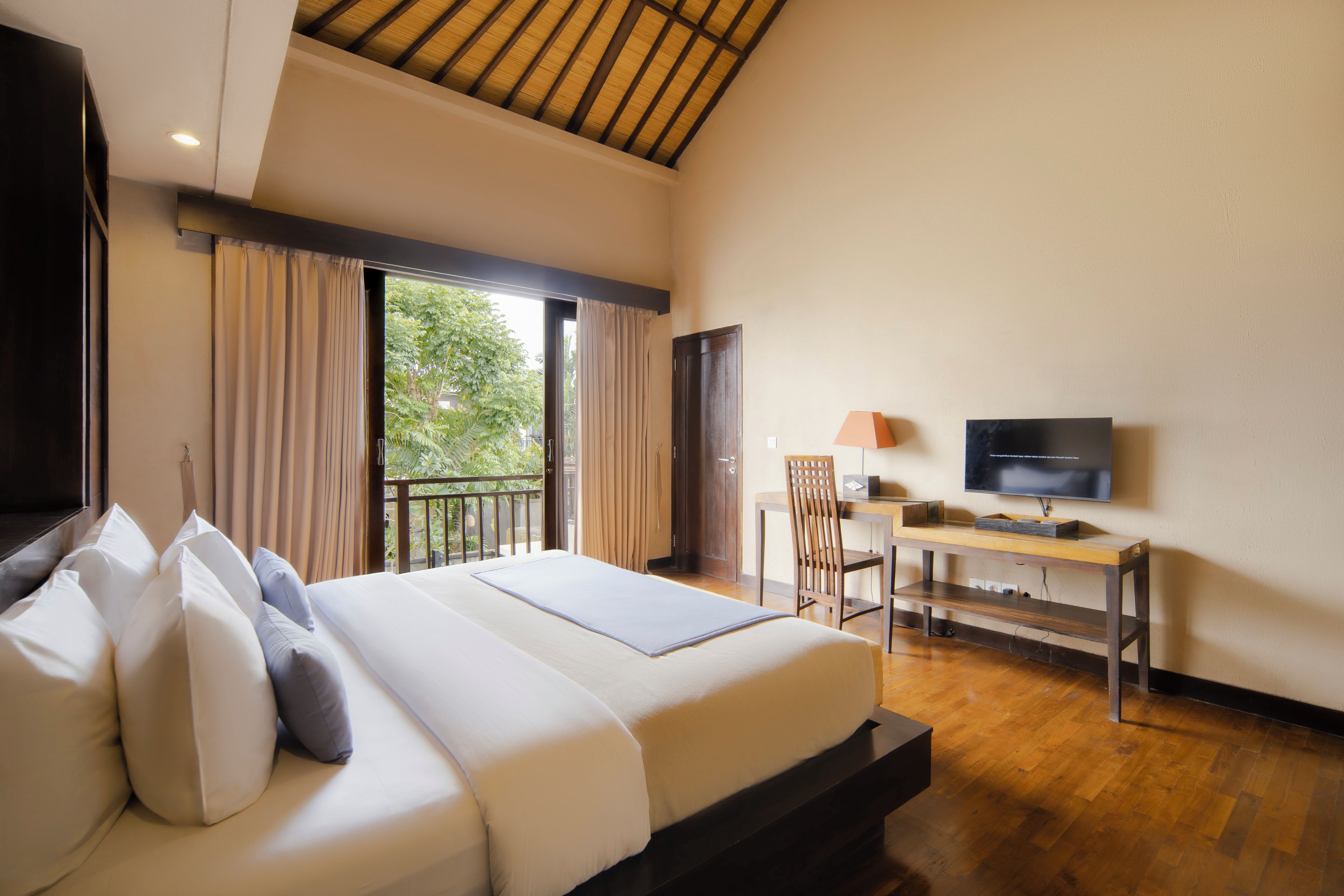 A hotel room with a bed, a desk, a TV, and a balcony with curtains.
