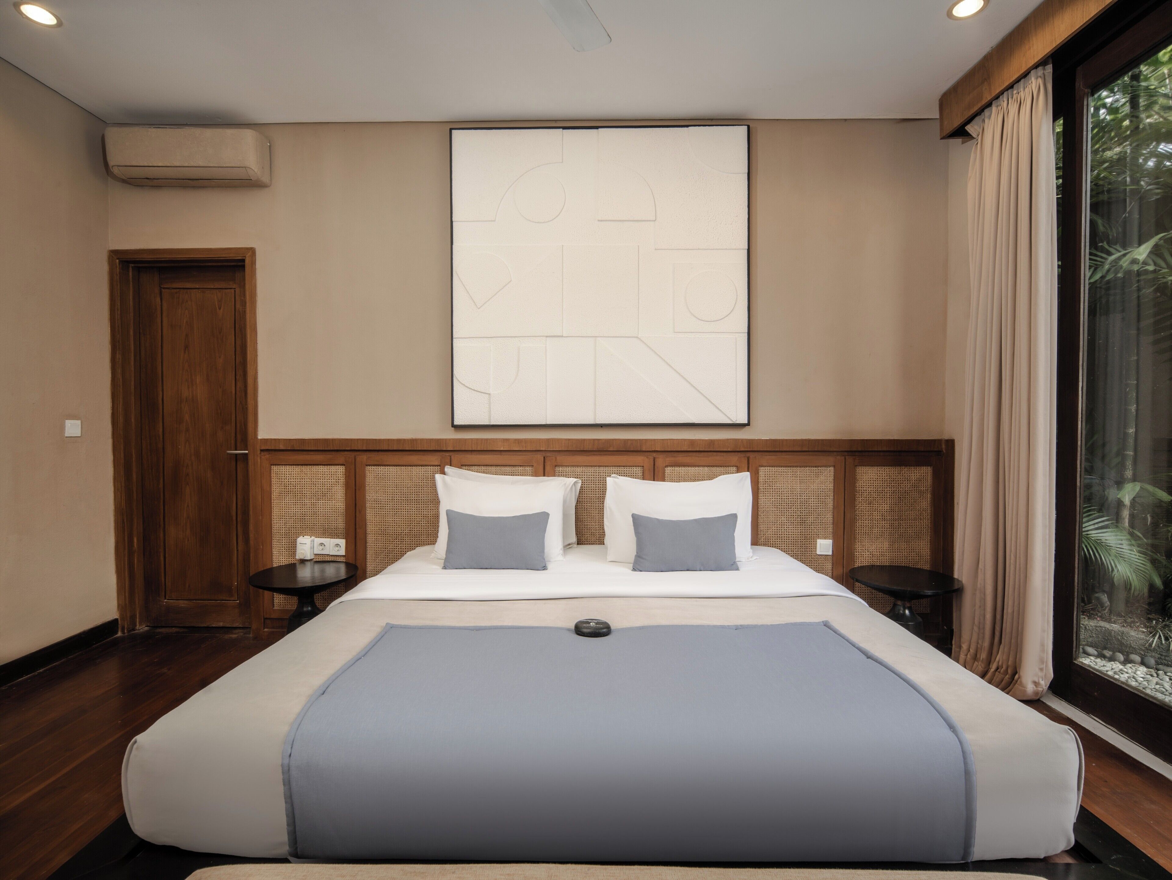 Habitación de hotel con una cama grande, una obra de arte colgada en la pared, una puerta de madera y una ventana con cortinas.