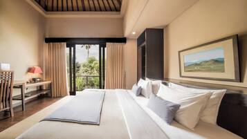 A hotel room with a large bed, a desk with a lamp, a painting on the wall, and a view of greenery through the window.