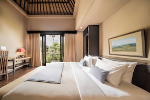 Habitació d'hotel amb un llit gran, un escriptori amb una làmpada, un quadre a la paret i vista a vegetació per la finestra.