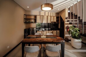 A modern kitchen with a wooden dining table, chairs, and a large potted plant.