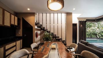Un interior moderno con una mesa de comedor de madera, sillas, una escalera, un televisor y vistas a una piscina.