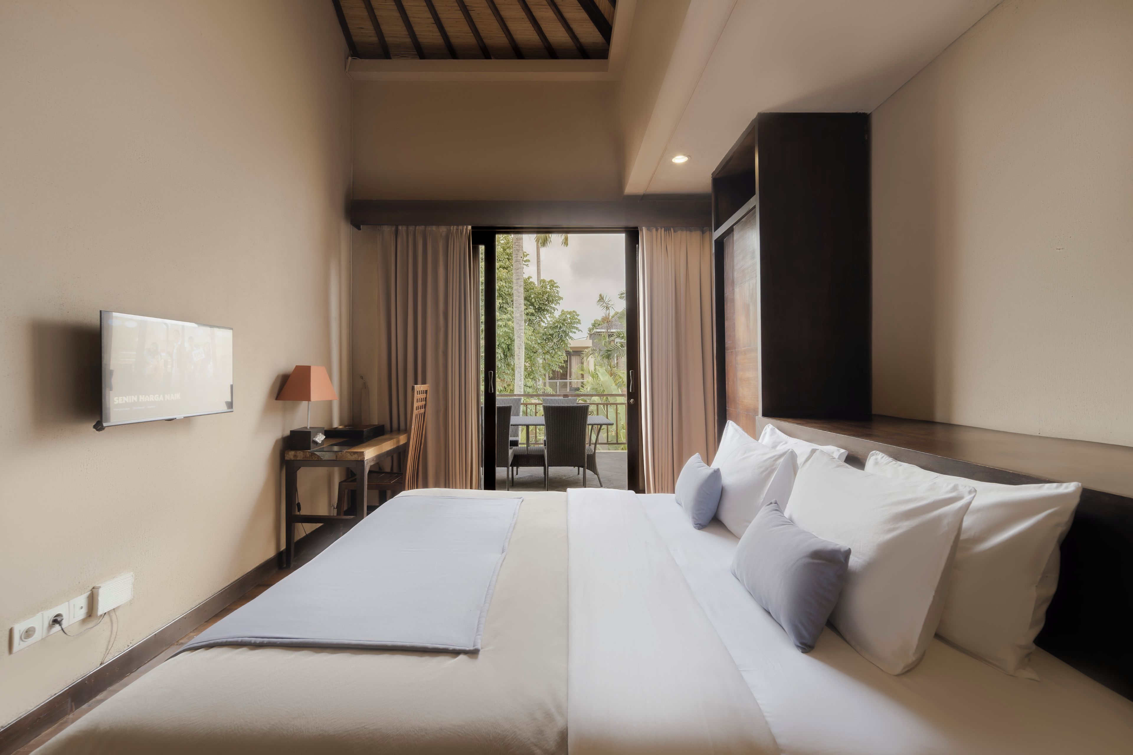 A hotel room with a bed, a TV, a desk, and a view of the outdoors.