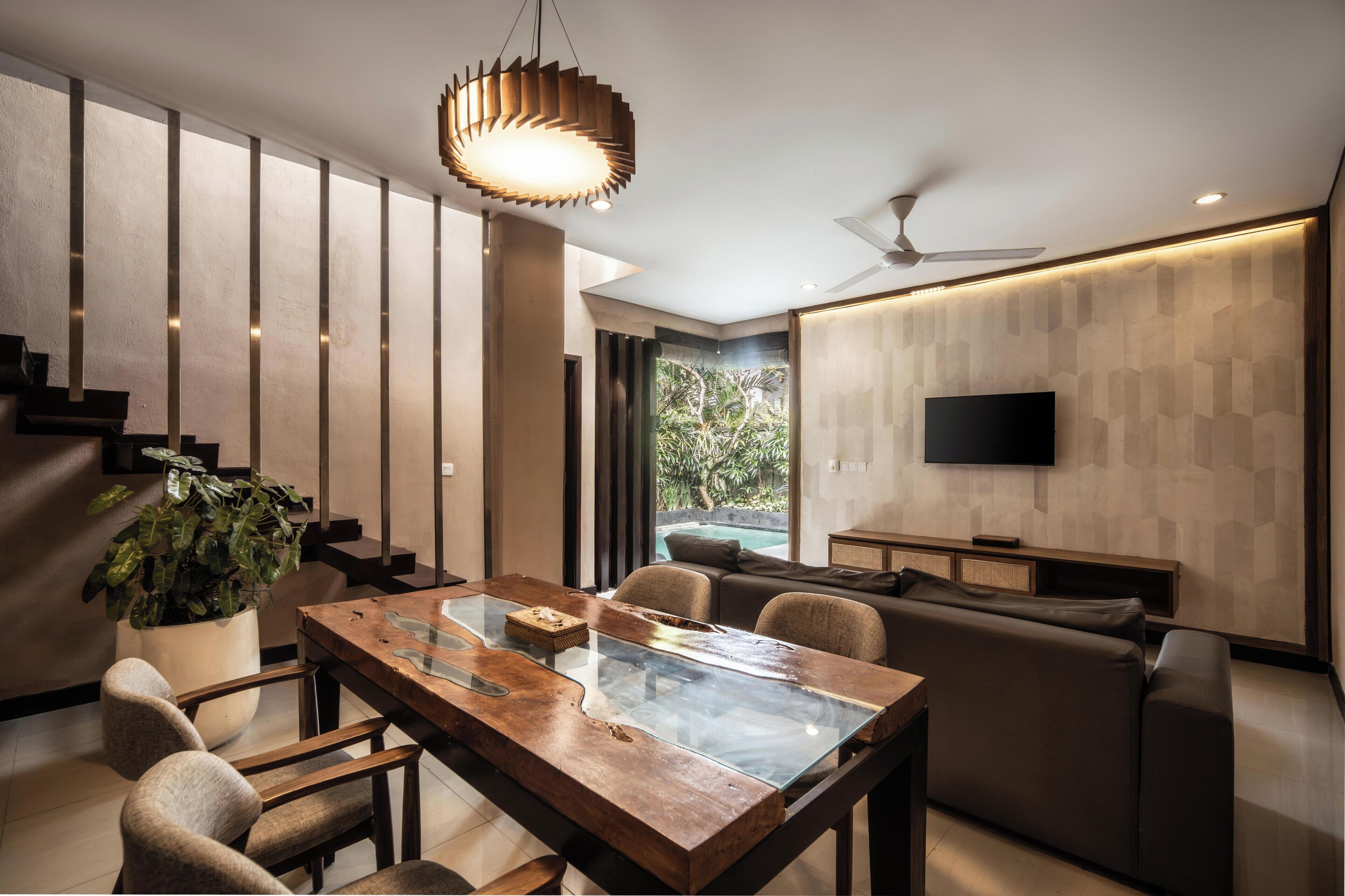 A modern living room with a wooden dining table, comfortable seating, a flat-screen TV, and a staircase leading to another level.