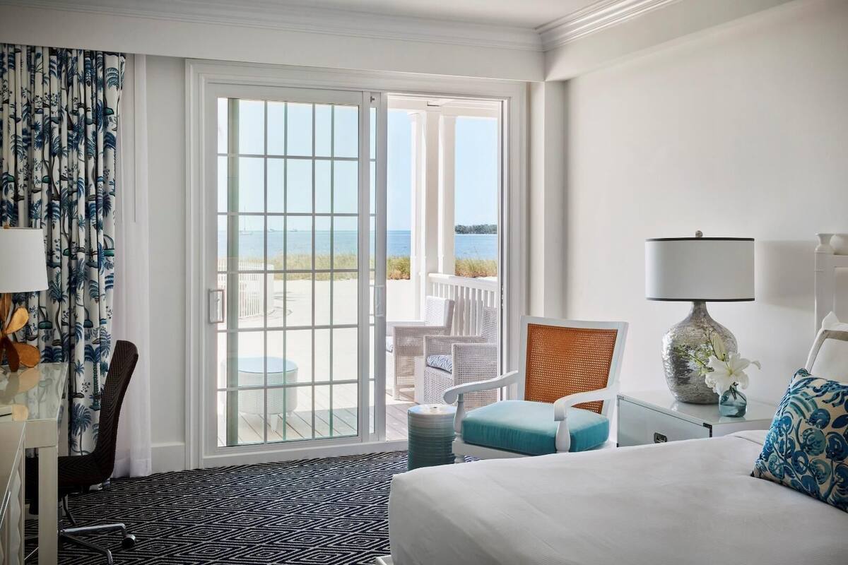 Une chambre d’hôtel avec un lit, un bureau, une chaise, une lampe et une vue sur la plage.