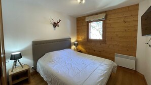 Une chambre à coucher avec un lit, une table de chevet avec une lampe, une tête de cerf décorative fixée au mur, une fenêtre donnant sur la verdure et un radiateur mural.