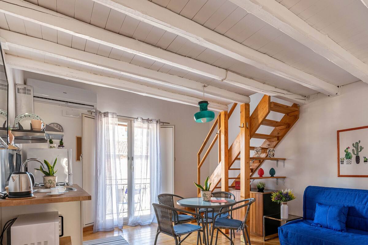 A cozy living area with a blue sofa, wooden staircase, and a dining table with chairs.