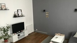 Una sala moderna con un televisor de pantalla plana, una consola blanca, un sofá gris, una mesita auxiliar pequeña y un letrero decorativo en la pared.