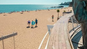 Una playa con un paseo marítimo de madera, un cartel que dice 'Plage de Monsieur Hulot' y una estatua de un hombre.