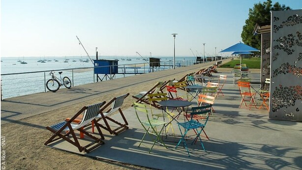 Un paseo marítimo con sillas y mesas de playa, una bicicleta y una torre de salvavidas.