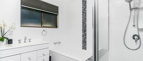 A modern bathroom with a white vanity, a glass shower enclosure, and a window with blinds.