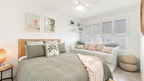 A bedroom with a bed, a bench, and a window with blinds.