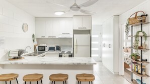 A modern kitchen with white cabinets, a marble countertop, a built-in oven, and a refrigerator. There are four wooden stools at the counter.