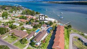 An aerial view of a coastal residential area with houses, a swimming pool, and boats on the water.