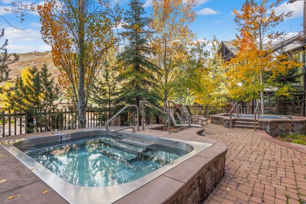 Un bain à remous entouré d’une terrasse en briques, avec une piscine en arrière-plan.