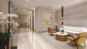 Un hall d’entrée moderne avec un sol en marbre, un canapé, deux fauteuils, une table basse et un grand tableau abstrait.
