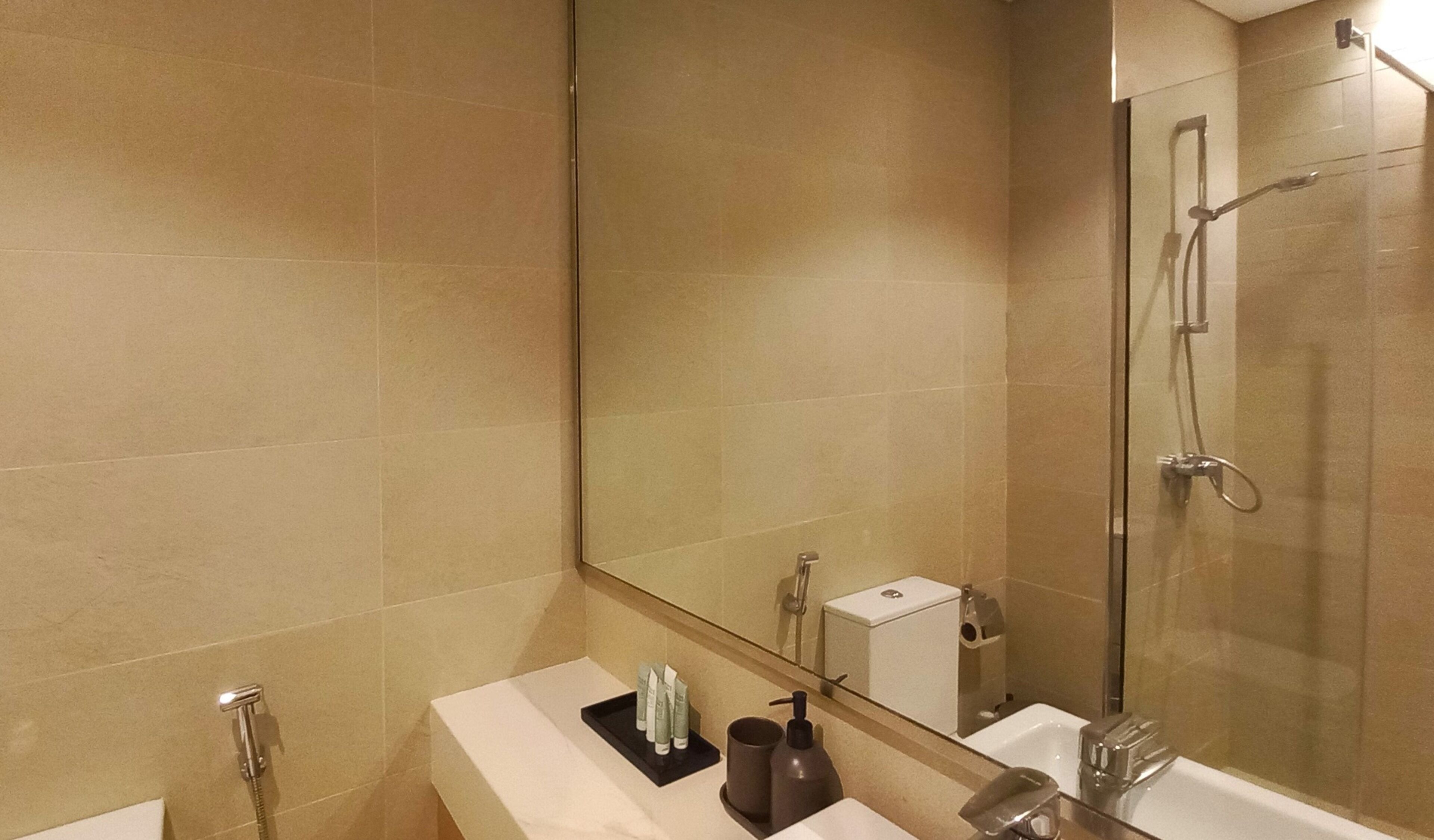 Een moderne badkamer met een douchecabine van glas, een grote spiegel en een wastafel met toiletartikelen.