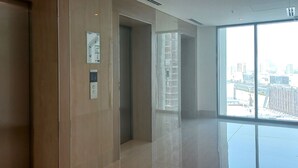 Un ascenseur moderne doté d’un écran numérique, un couloir avec un mur en verre et une vue sur le paysage urbain.