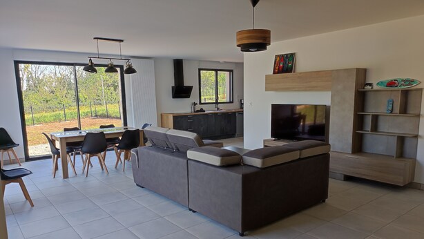 A modern living room with a large L-shaped sofa, a dining table with chairs, a TV, and a wooden TV stand. - Villa a Angles (Angles)