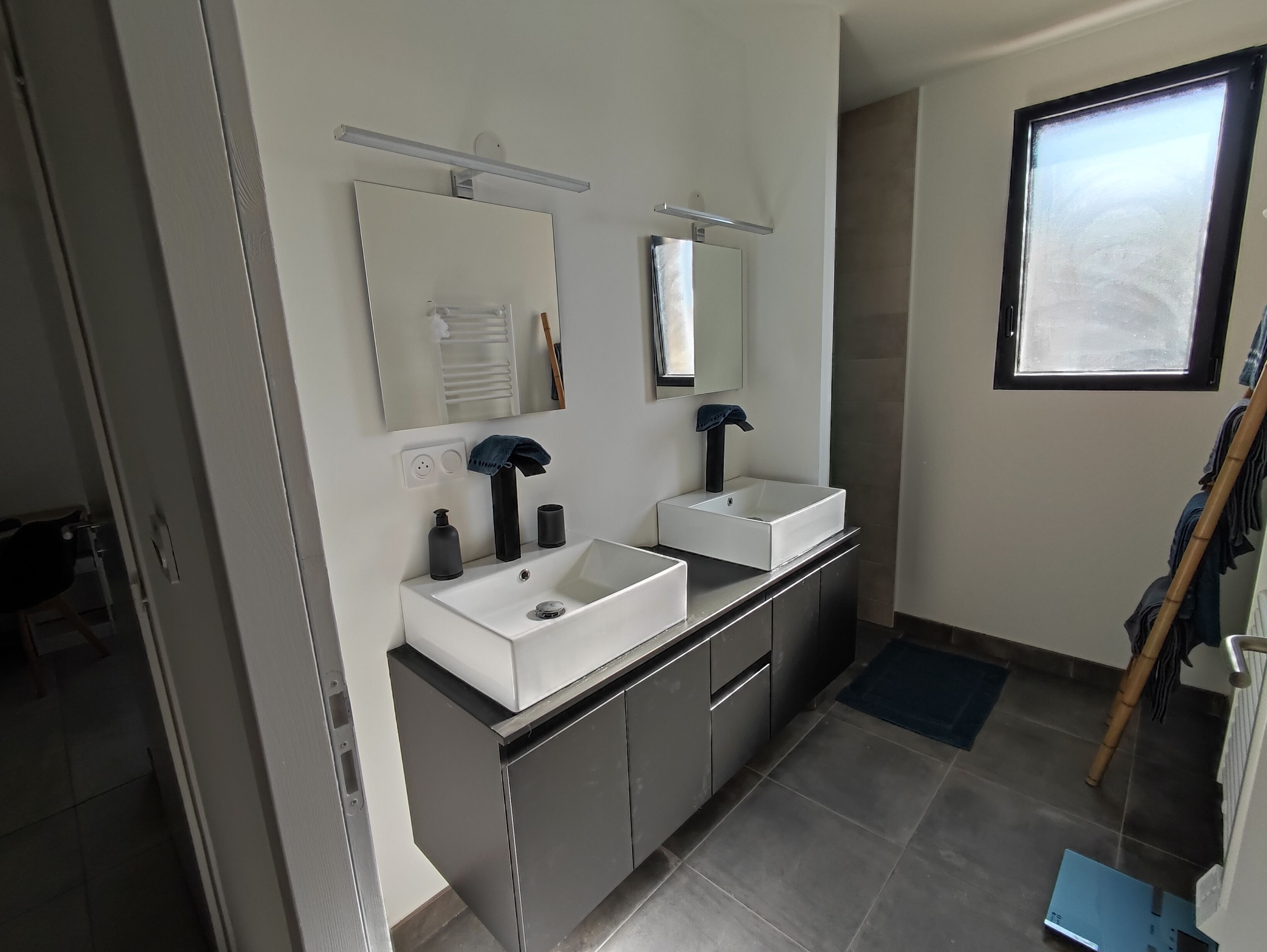 Une salle de bain moderne avec deux lavabos, un miroir et une fenêtre.