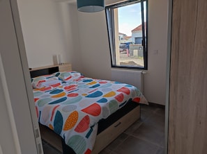 A bedroom with a bed, a bedside table, a window, and a radiator.