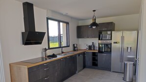 A modern kitchen with a large island, stainless steel appliances, and a window providing a view of the outdoors. - Villa a Angles (Angles)