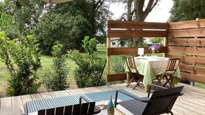 A wooden deck with a table and chairs, surrounded by greenery and trees. - Le Chalet Kbaia Océan et Calme (Saint-Julien-en-Born)