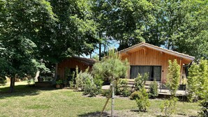 A wooden cabin with a deck, surrounded by trees and a grassy area. - Le Chalet Kbaia Océan et Calme (Saint-Julien-en-Born)