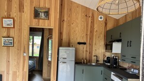 A compact kitchen with wooden walls, a refrigerator, and basic appliances. - Le Chalet Kbaia Océan et Calme (Saint-Julien-en-Born)