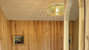 A wooden-paneled room with a bed, a nightstand, a lamp, and a mirror. - Le Chalet Kbaia Océan et Calme (Saint-Julien-en-Born)