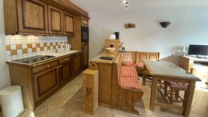 A kitchen with wooden cabinets, a stove, a sink, and a dining area with a table and chairs.