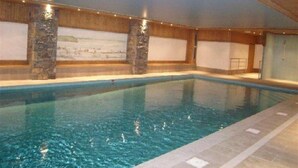 An indoor swimming pool with stone pillars, tiled flooring, and a mural on the wall.