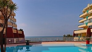 A swimming pool with clear blue water, surrounded by a poolside area with lounge chairs. - Seafront apartment for 4 in Sète with private parking (Sète)