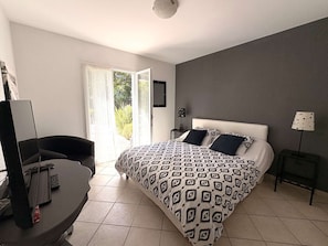 A bedroom with a bed, a desk, a chair, a TV, and a window with curtains.