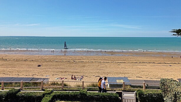 A beach with a clear sky, a sailboat, and people relaxing on the sand. - Apartment with balcony, garden, and beach access (Jullouville)
