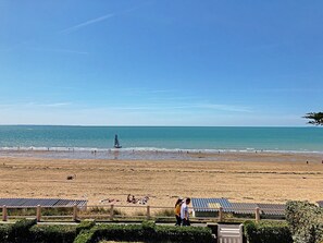 Una playa con cielo despejado, un velero y gente relajándose en la arena.