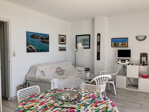 Una sala de estar acogedora con sofá, una mesa de comedor con mantel colorido, televisor y varias decoraciones en las paredes.