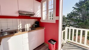 A compact kitchen with white cabinets, a stainless steel sink, and a red trash bin. - Apartment with balcony, garden, and beach access (Jullouville)