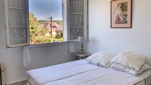 A bedroom with a bed, a nightstand, a lamp, and a window with curtains. - Apartment with balcony, garden, and beach access (Jullouville)