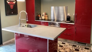 A modern kitchen with red cabinets, stainless steel appliances, and pendant lighting.
