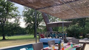 An outdoor dining area with wicker chairs and a pool table, surrounded by a wooden deck and a covered seating area.