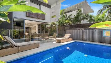 A modern house with a swimming pool, outdoor furniture, and tropical plants.