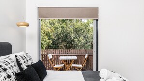A bedroom with a bed, a small table, two chairs, a wooden fence, and a view of trees. - Kokos 3 - Beach Houses of Byron (Byron Bay)