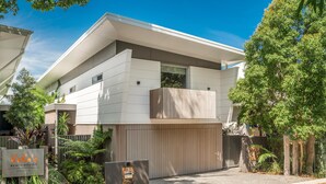 A modern two-story house with a flat roof, a balcony, and a gated driveway. - Kokos 3 - Beach Houses of Byron (Byron Bay)