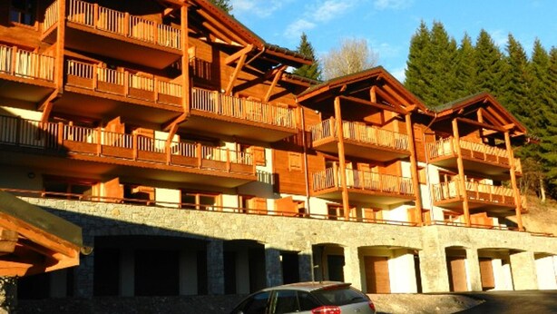 A multi-story wooden building with balconies, likely a hotel or lodge, with a stone base and a parking area in front.