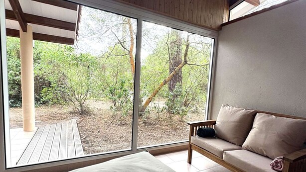 Ein Zimmer mit einer großen SchiebeglasTür, die zu einem Außenbereich mit Bäumen und einer Holzterrasse führt.